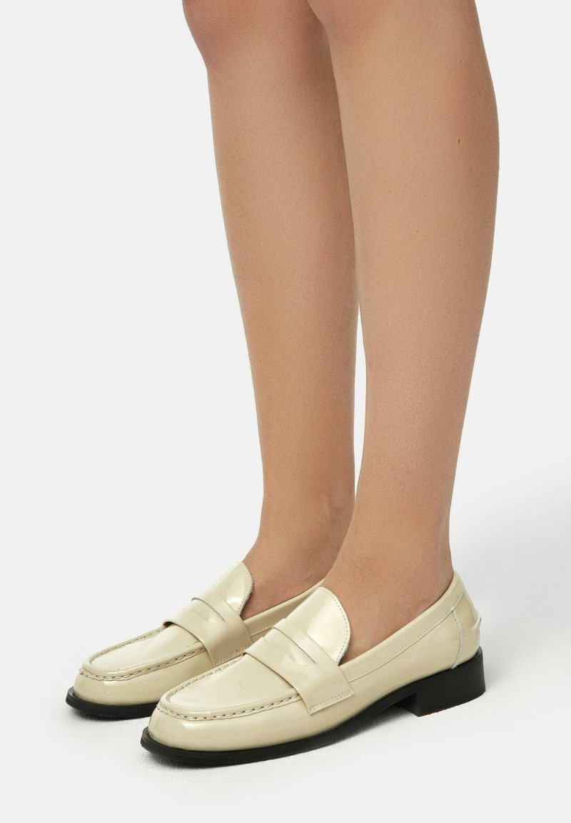 Cream patent leather loafers with a square toe and low black heel, featuring a smooth finish and subtle stitching details.