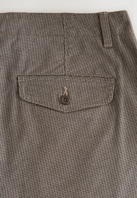 Braun- und beige karierte Stoff mit einer Gesäßtasche, die einen einzelnen braunen Knopf, verstärkte Nähte und eine glatte Textur aufweist.