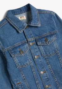 Chaqueta de denim en azul claro con un cuello clásico, dos bolsillos en el pecho, botones plateados y detalles de costura naranja.