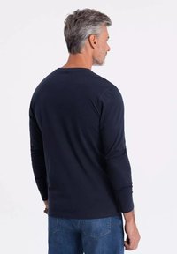 Námořnické tričko s dlouhým rukávem vyrobené z měkké látky, s kulatým výstřihem a uvolněným střihem. S kombinací modrých džínů.