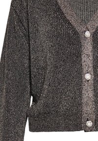 Mustakalla ja hopea metallinen neulecardigan, jossa on V-pääntie, pitkät hihat ja koristepainikkeita. Varusteena ribbaus hihansuissa ja helmassa.