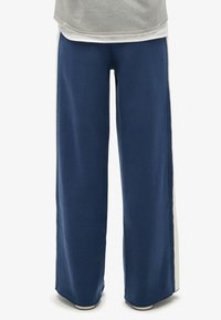 Marineblauwe wijde trainingsbroek met een zachte textuur en crèmekleurige zijkanten. Beschikt over een elastische tailleband voor extra comfort.