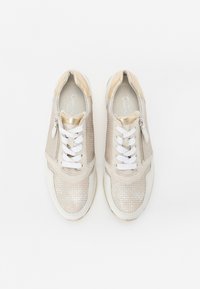 Sneakers beige con una toma in mesh testurizzato, lacci bianchi e un accento dorato. Presentano una zip laterale e una suola ammortizzata.