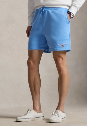 Svetlomodré fleecové šortky s nastaviteľným pásom na šnúrku, s malým vyšívaným logom na dolnej ľavej strane. Nosené s bielymi topánkami.
