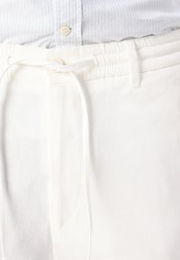 Shorts en lin blanc avec un cordon de serrage à la taille, présentant une texture lisse et des poches latérales. La taille est élastique pour un confort optimal.