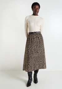 Top de manga larga de canalé beige con costura en forma de V, combinado con una falda midi de estampado de leopardo y botas negras de tacón. Un cinturón negro resalta la cintura.