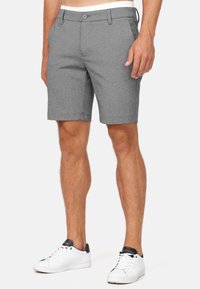Grijze shorts van een gestructureerde stof, met een knoopsluiting aan de voorkant en zijzakken. Draagt samen met witte sneakers en een contrasterende tailleband.