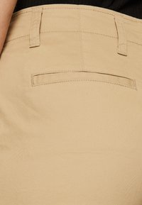 Beige Hosen aus einem glatten, strukturierten Stoff, mit einer kleinen Gesäßtasche und einer schlanken, maßgeschneiderten Passform.