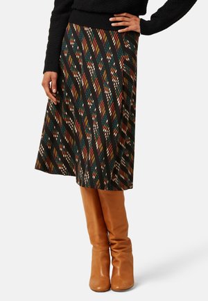 Mujer con falda a la rodilla de patrón geométrico multicolor, suéter negro y botas de cuero marrón claro hasta la rodilla.
