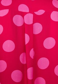 Fuchsia tyg med stora rosa prickar. Designen har en mjuk textur och veck, vilket skapar en mjuk draperad effekt.