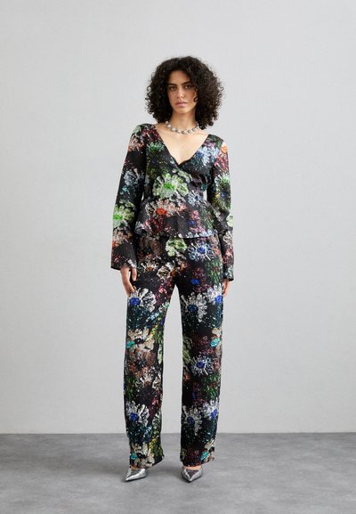 Ensemble à imprimé floral avec un fond noir, des manches longues et une silhouette peplum. Tissu texturé avec des couleurs vives. Chaussures argentées.
