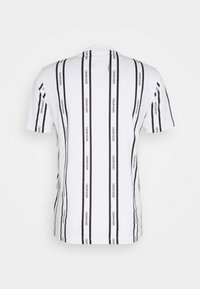 Bílý tričko s krátkým rukávem s vertikálními černými pruhy, na kterém je opakovaný text "CALVIN KLEIN". Je vyrobeno z bavlny, má hladkou texturu.