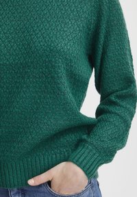 Maglione verde con texture, colletto rotondo, polsini e orlo a coste. Il tessuto presenta un motivo a maglia diagonale e una vestibilità comoda.