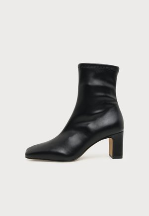Stivaletto nero in pelle con punta quadrata e tacco a blocco su sfondo semplice.