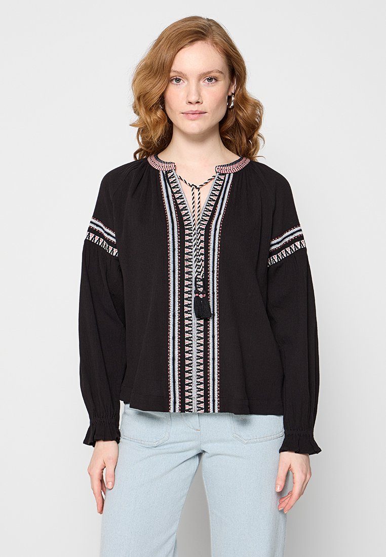 Schwarze bestickte Bluse mit langen Ärmeln, die eine gemusterte Vorderseite, Quasten-Details und eine lockere Passform aufweist.