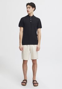 Svart ribbet polo-skjorte med korte ermer, tre-knappers knappestolpe, parret med beige linshorts og brune sandaler. Minimalistisk design.