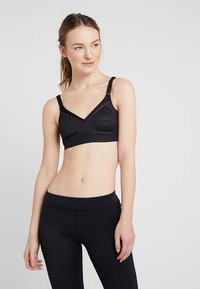 Svart sports-bh med teksturert design, V-hals-form, justerbare stropper og svak rosa aksent ved halsen. Brukt med svarte leggings.