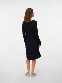 Czarna prążkowana sukienka z długimi rękawami, dopasowanym gorsetem i rozkloszowanym dołem. Gładka faktura, długość do kolan, w komplecie z jasnobeżowymi płaskimi butami.