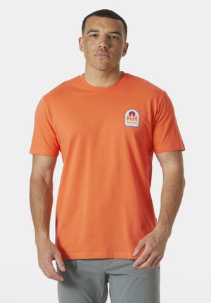 Korte mouwen, ronde hals t-shirt in feloranje katoen, met een blauw-wit logo patch op de linkerkant van de borst. Soepele textuur.