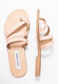 Beige flade sandaler med tre tynde strukturerede stropper over foden, en der snor sig omkring storetåen, og en glat sål.