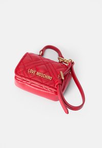 Raudona kvadratinė dirbtinės odos rankinė su auksiniu "LOVE MOSCHINO" logotipu, trumpu viršutiniu rankenėle ir nuimama petneša.