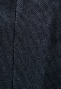 Tissu texturé bleu foncé avec un motif tissé, présentant une surface légèrement rugueuse et des variations de couleur subtiles. Comprend des détails de couture.
