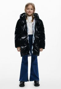 Sort, blank pufferjakke med hætte, der har et farverigt inderside. Sammen med blå, flagrende jeans og sorte platform-sko.