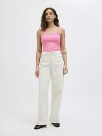 Rosa figurnära linne med fyrkantig halsringning, kombinerat med vita vida byxor med hög midja. Svarta högklackade skor med meshdetaljer.