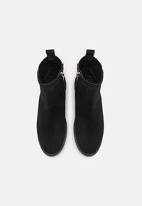 Stivaletti neri in suede con una texture liscia, dettagli in pelle, cerniere laterali e linguette sul colletto per un facile indossamento.