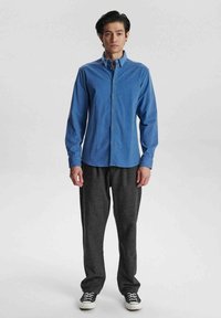Camisa azul de botones con mangas largas y botones dorados, combinada con pantalones relajados de color gris oscuro y zapatillas negras.