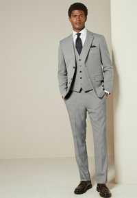 Light grey three-piece suit with a notched lapel, single-breasted jacket, matching waistcoat, and flat-front trousers. Dark shoes accent the outfit.