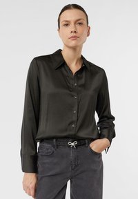 Czarna satynowa koszula na guziki z klasycznym kołnierzykiem, długimi rękawami i czarnymi guzikami, zestawiona z ciemnoszarymi dżinsami i czarnym paskiem.