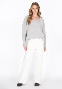 Grauer Strickpullover mit V-Ausschnitt, lockerer Passform und überschnittenen Schultern, kombiniert mit weißen weit geschnittenen Hosen und schwarzen Schuhen. Schlichtes Design.
