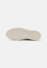 Rubber sneaker sole in off-white with zigzag and diamond tread patterns. Features brand logo near heel and textured edges for grip.