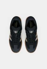 Black and gray sneakers with a textured surface, featuring three white stripes, round laces, and a gum sole. adidas logo on the tongue.