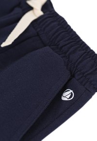 Λαδί μπλε βαμβακερό παντελόνι με ελαστική μέση και εκρού κορδόνι σύσφιξης. Διαθέτει μικρό λευκό λογότυπο στην αριστερή πλευρά κοντά στην τσέπη.