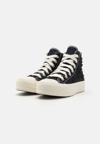 Czarne wysokie sneakersy z białymi sznurówkami i grubymi białymi podeszwami, z haftowanymi kwiatowymi wzorami po zewnętrznych stronach.