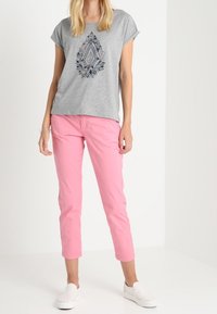 Grå kortärmad t-shirt med ett blått och svart geometriskt mönster, tillsammans med ljusrosa cropped byxor och vita slip-on skor.