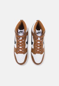 High-top sneakers featuring white leather with brown accents, textured brown tongue, black Swoosh logo, and brown laces.