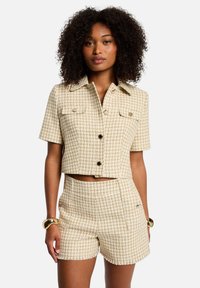 Veste courte beige et shorts assortis en motif pied-de-poule. Dotée de deux poches poitrine et de boutons noirs. Tissu texturé avec une coupe structurée.