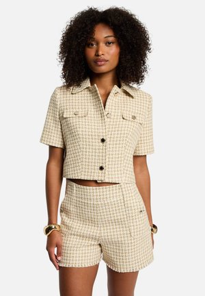 Veste courte beige et shorts assortis en motif pied-de-poule. Dotée de deux poches poitrine et de boutons noirs. Tissu texturé avec une coupe structurée.
