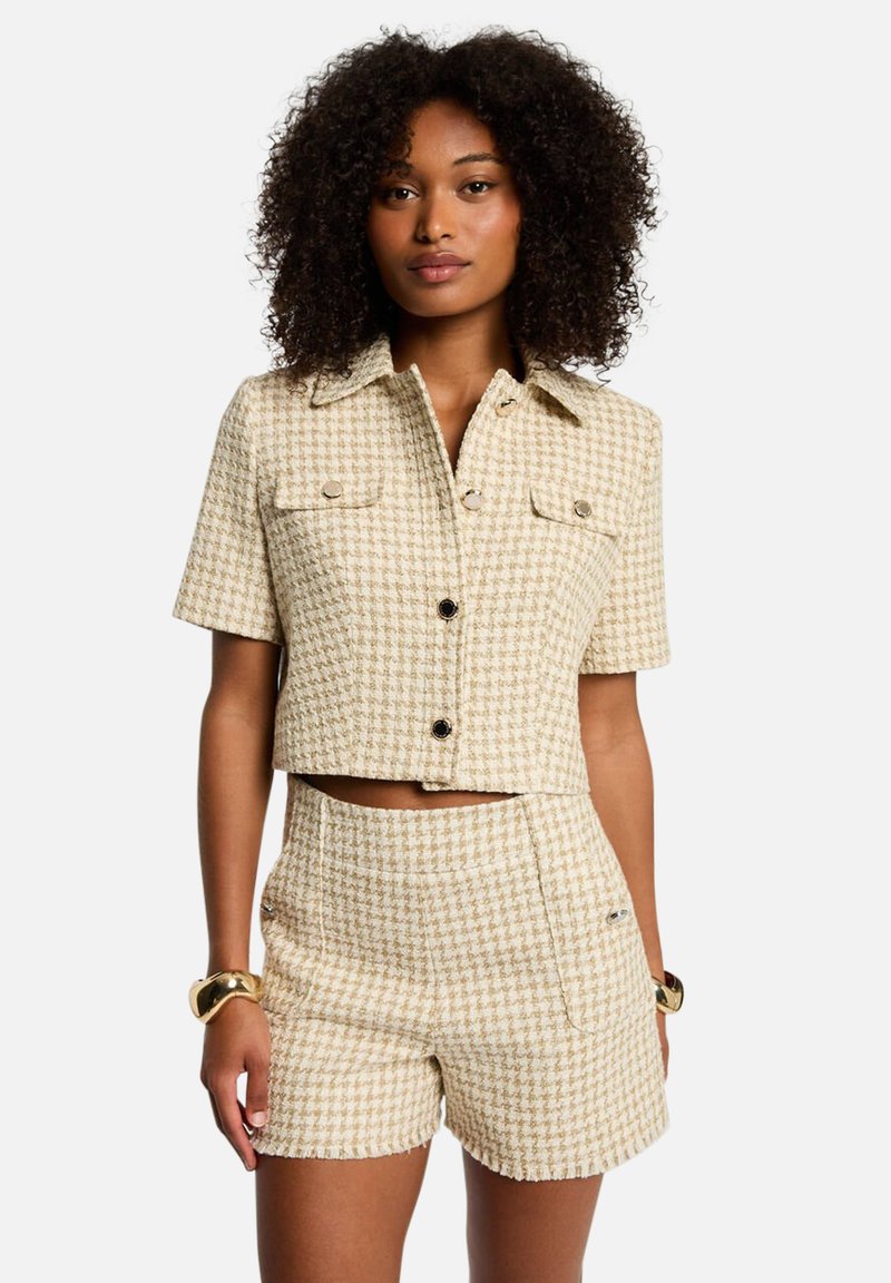 Veste courte beige et shorts assortis en motif pied-de-poule. Dotée de deux poches poitrine et de boutons noirs. Tissu texturé avec une coupe structurée.