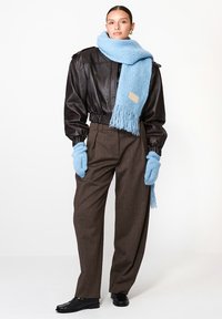 Juodas odinis sutrumpintas švarkas, rudos tekstūruotos kelnės, šviesiai mėlyna megzta šalikas su kutais ir atitinkantys mėlyni pirštinės. Juodi batai užbaigia aprangą.