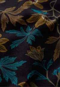 Tkanina sztruksowa z kwiatowym wzorem, prezentująca brązowe i turkusowe liście na ciemnym tle, ukazująca teksturowaną, tkanią strukturę.
