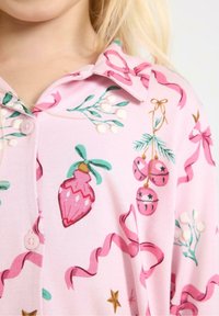 Rosa Baumwollbluse mit festlichen Mustern aus Ornamenten, Bändern und Grünpflanzen. Mit Knöpfen und einem Kragen-Design verziert.