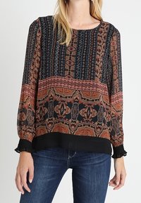 Blusa a maniche lunghe con un design a motivi in tonalità terrose di arancione e nero, con maniche testurizzate e orlo nero uniforme.
