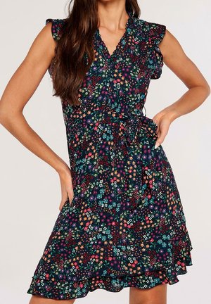 Frau trägt ein ärmelloses, dunkelfarbenes Kleid mit kleinem, mehrfarbigem Blumenmuster, gerafften Ärmeln und einem gebundenen Taillengürtel.