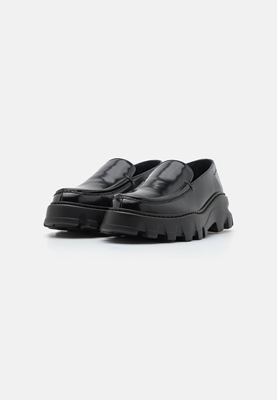 Chaussures noires à enfiler avec une finition brillante, semelle épaisse crantée, bout rond et minimalisme dans les détails de couture. Texture en cuir lisse.