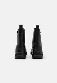Botas de tobillo de cuero negro con un acabado suave, que cuentan con una suela de goma texturizada y pestañas en la parte trasera para facilitar su uso.