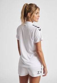 Maglietta sportiva bianca e pantaloni corti realizzati in tessuto leggero. La maglietta presenta strisce nere di accento sulle spalle e il logo sui pantaloni corti.
